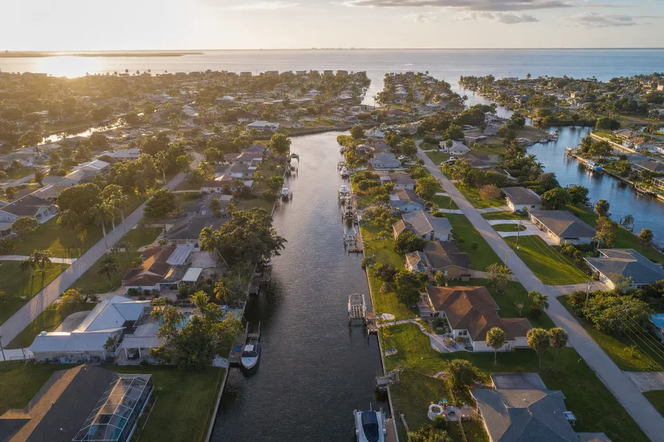 Aerial view of a canal-front residential neighborhood in southwest Florida at golden hour, with docks and palms along the water.