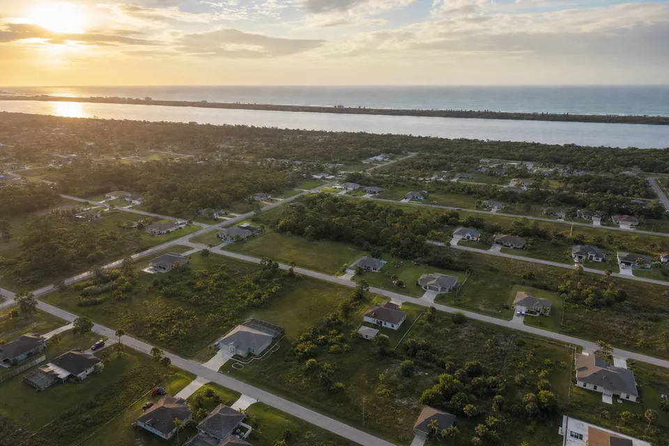 Aerial view of a growing residential neighborhood on Florida's Space Coast at golden hour, with the lagoon and barrier island in the distance.